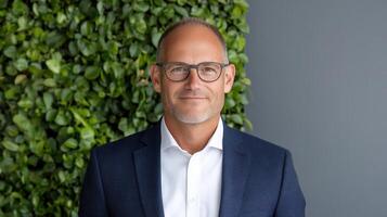 A man in glasses and a suit standing in front of a green wall photo