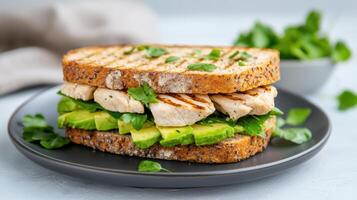 Grilled chicken sandwich with avocado and cilantro on a black plate photo