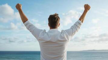A man with his arms up in the air looking at the ocean photo