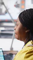 Vertical Black factory employee oversees solar system performance at desk seated beside production line machines. Female technician analyzes solar energy flow and updates system software. Camera A. video