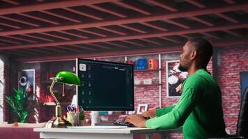 African American worker using program with photos in a modern loft. Young man creating visual content with deep learning models and prompts on monitor with AI interface. Camera A. video