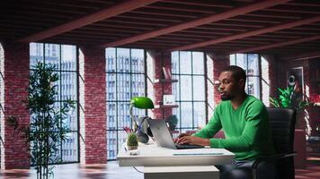 Focused male freelancer browsing web on laptop in a modern studio loft, demonstrating a lifestyle of independence, connection and productivity in a virtual workspace. Man multitasking. Camera B. video