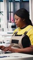 Vertical Technician monitors manufacturing data on pc in solar panel factory, employee finetunes equipment settings to support efficient solar power production. Woman seated next to assembly line. Camera A. video