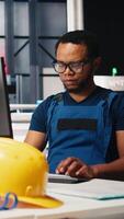 Vertical Black engineer runs diagnostic checks on solar panel assembly software, optimizing the production process and solar cells designs for alternative energy. High tech modern factory. Camera B. video
