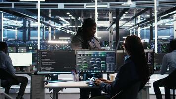 Data center manager supervising technician using node tree software to analyze datasets. Server room team leader oversees IT expert using visual programming tools to improve gear performance, camera A video
