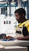 Vertical Black worker programming robotic assembly line in solar cell factory, working with high tech software for automation. Male engineer testing photovoltaic system, machinery. Camera B. video