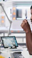 Vertical African american technician evaluates renewable energy metrics at pc station, using advanced monitoring and manufacturing tools. Engineer improves solar power system accuracy. Camera A. video