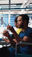 Vertical African american wheelchair user working in solar panel factory, optimizing systems for renewable energy. Engineer examines robot arms automation in a disability friendly power plant. Camera B. video