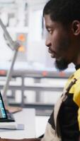 Vertical Black worker programming robotic assembly line in solar cell factory, working with high tech software for automation. Male engineer testing photovoltaic system, machinery. Camera A. video
