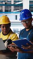 Vertical All black inspectors team in photovoltaics factory look over documents, review performance of robot arms placing solar panels on assembly lines. Supervisors inspecting solar cells plant. Camera A. video