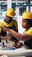 Vertical African american workers checking up on manufacturing equipment in solar panel factory, reading documentation files. Team of engineers in industrial facility inspecting production process. Camera B. video
