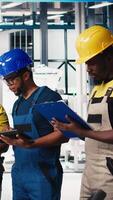 Vertical Group of black employees at the solar panels factory reviewing data on devices and documents. Photovoltaics facility engineers working on innovative solar cells design prototype. Camera B. video