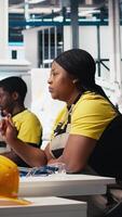 Vertical African american engineer analyzes energy consumption software in solar factory, uses PC program to enhance solar cell production and reduce faults in automated machinery systems. Camera B. video