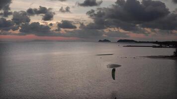 A solitary kitesurfer rides the calm twilight waters, their colorful kite against a breathtaking sunset sky with soft blues, warm pinks, and oranges, creating a peaceful coastal scene video