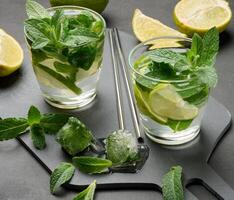 Glass of mojito cocktail with fresh mint leaves, lime slices, and ice cubes on a dark stone background. photo