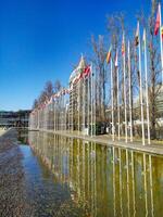 LISBON, PORTUGAL - JANUARY 17, 2025 Row of flags of different countries reflected in water, set against a modern building and a clear blue sky. photo