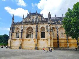 BATALHA, PORTUGAL - JUNE 10, 2023 View of the Batalha Monastery facade, a masterpiece of Gothic architecture, with ornate windows and stone details, under a blue sky. Tourism theme. photo