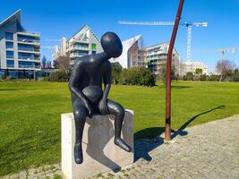 LISBON, PORTUGAL - JANUARY 17, 2025 Modern art sculpture in park setting. Abstract figure contemplates urban development. Symbolism of change, reflection, or solitude. photo