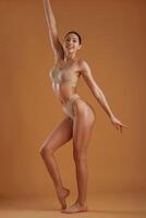 Orange, colored wall behind. Woman ,with slim body shape is posing against background photo