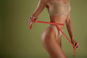 Results of diet, with measuring, tape. Woman with slim body shape is posing against background photo
