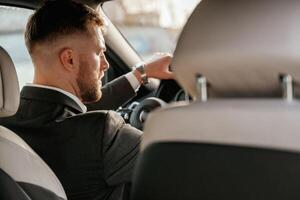 Driving, focused. Man in black suit is sitting in the car, driving. photo