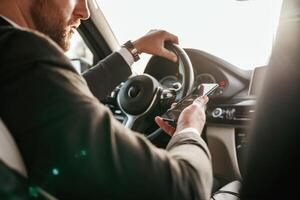 Surfing the internet by using smartphone..,, Man in black suit is sitting in the car, driving photo