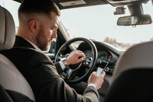 Surfing the internet ,by ,using smartphone. Man in black suit is sitting in the car, driving photo