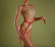 Results of diet, with measuring tape.. Woman with slim body shape is posing against background photo