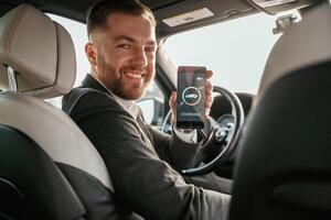 Monitoring charging process, app ,in, smartphone. Man in black suit is sitting in the car, driving photo