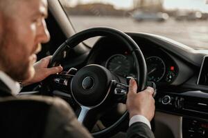Close up, view ,of steering wheel. Man in black suit is sitting in the car, driving photo