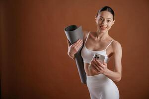 Smartphone and yoga mat in hands.., Beautiful fitness woman is in the studio photo