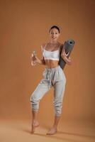 Looking, forward, holding bottle of water and mat. Beautiful fitness woman is in the studio photo