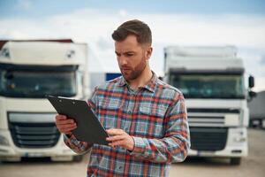 Having hard time reading the document in notepad. Man is standing against trucks outdoors photo
