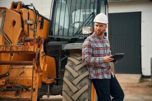 Digital, tablet, in hands. Man is with tractor. Agricultural worker photo