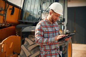 Digital tablet in hands. Man ,is with, tractor. Agricultural worker photo