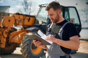 Data in the notepad, reading. Man is, with tractor. Agricultural worker photo