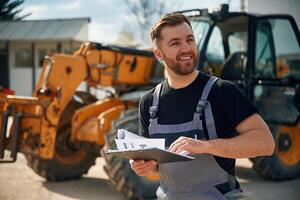 Data, in the notepad, reading. Man is with tractor. Agricultural worker photo