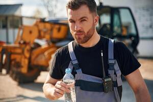 Drinking water, taking a break, tired.,.. Man is with tractor. Agricultural worker photo