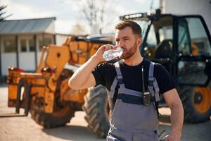 Drinking water, taking a break, tired.. Man is with tractor. Agricultural worker photo