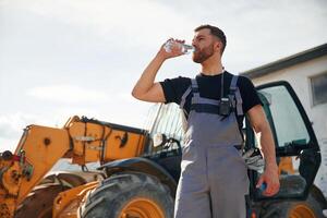 Drinking water, taking a break,, tired. Man is with tractor. Agricultural worker photo