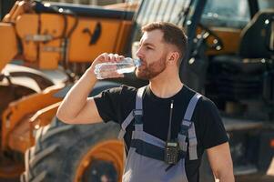 Bottle of water, drinking,, taking a break. Man is with tractor. Agricultural worker photo