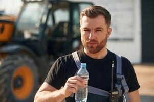 Bottle of water, drinking, taking, a break. Man is with tractor. Agricultural worker photo
