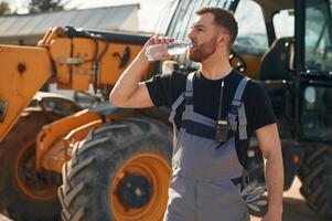 Bottle of, water, drinking, taking a break. Man is with tractor. Agricultural worker photo