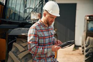 Digital tablet in, hands. Man is with tractor. Agricultural worker photo