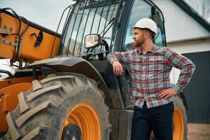 Leaning, on the vehicle. Man is with tractor. Agricultural worker photo