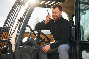 Walkie, talkie device, conversation, orders. Man is with tractor. Agricultural worker photo