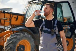 Drinking, water, taking a break, tired. Man is with tractor. Agricultural worker photo