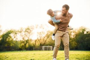 Wellbeing, kid is on the shoulders or back. Happy father with son are having fun on the field at summertime.. photo
