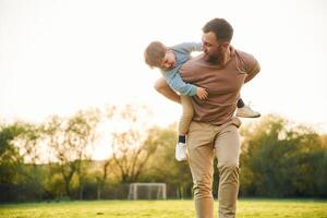 Wellbeing,, kid, is ,on the shoulders or back. Happy father with son are having fun on the field at summertime photo