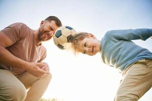 Soccer ball, holding ,it ,by heads, fun. Happy father with son are on the field at summertime photo